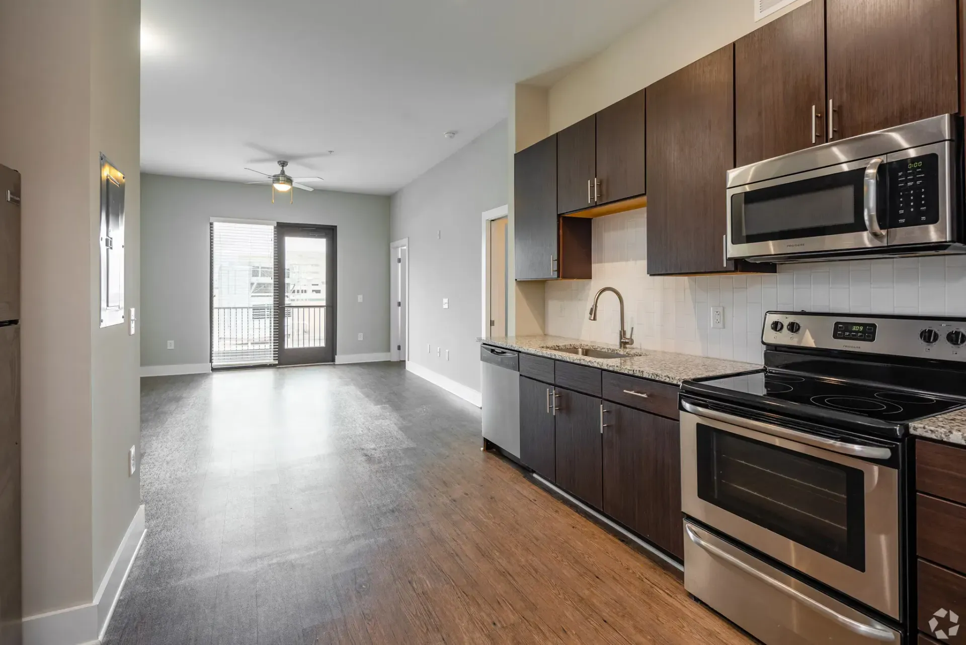 Modern apartment kitchen with dark wood cabinets, granite counters, and stainless steel appliances.