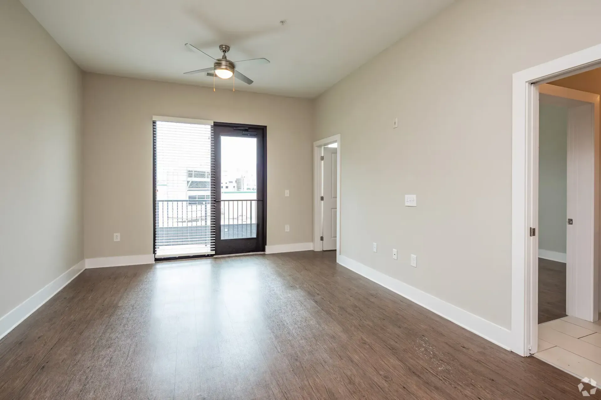 Living room with beige walls, wood-look flooring, a ceiling fan, and a balcony door with blinds.