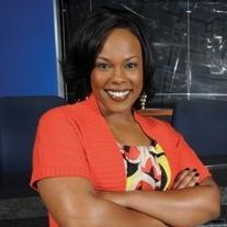 A woman in a red sweater is smiling with her arms crossed.