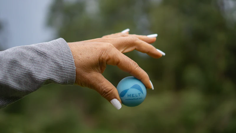 Hand hält MELT Therapieball für fasziale Selbstmassage und Regeneration