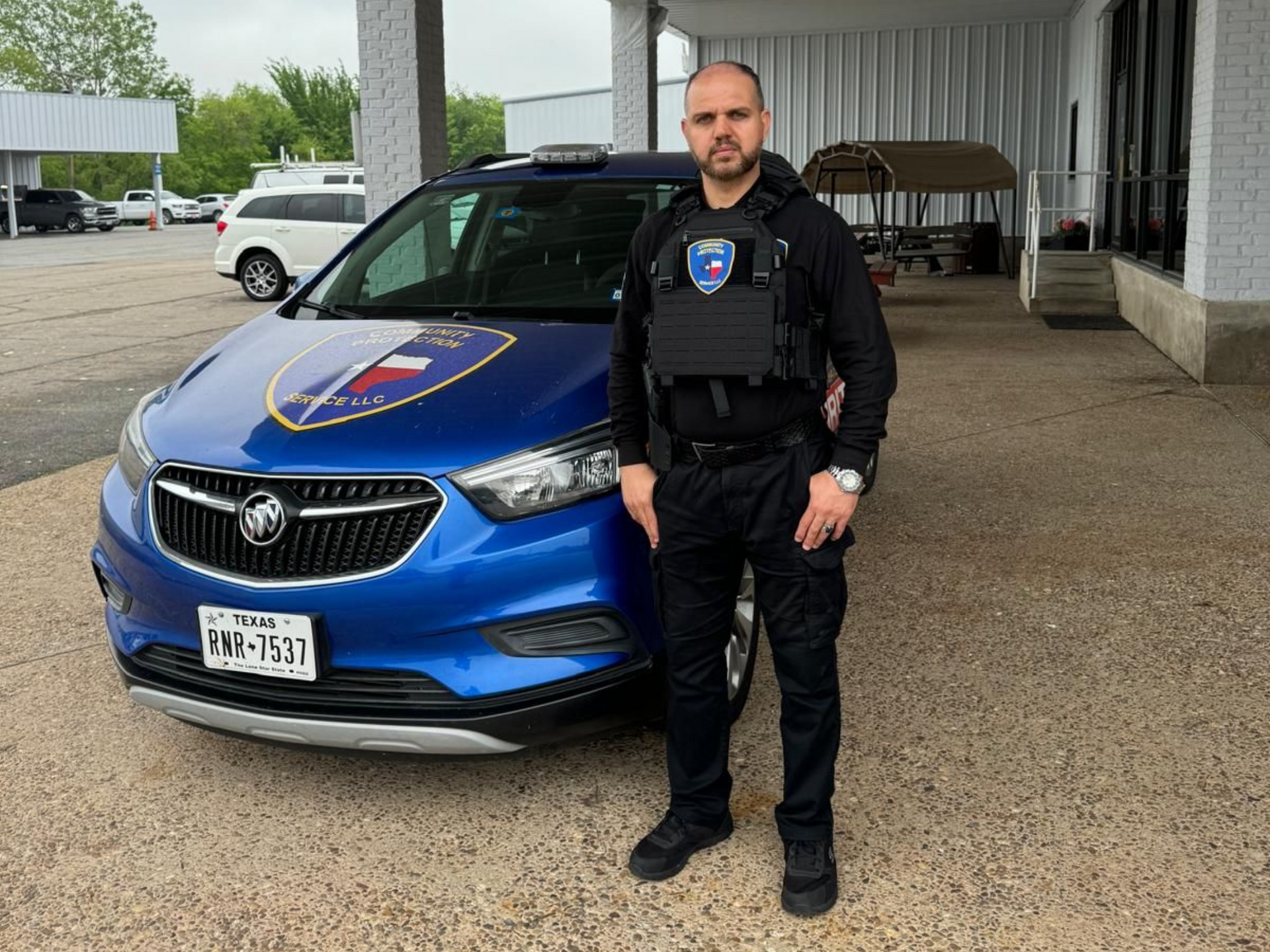 Police officer standing in front of a blue patrol car under a covered area