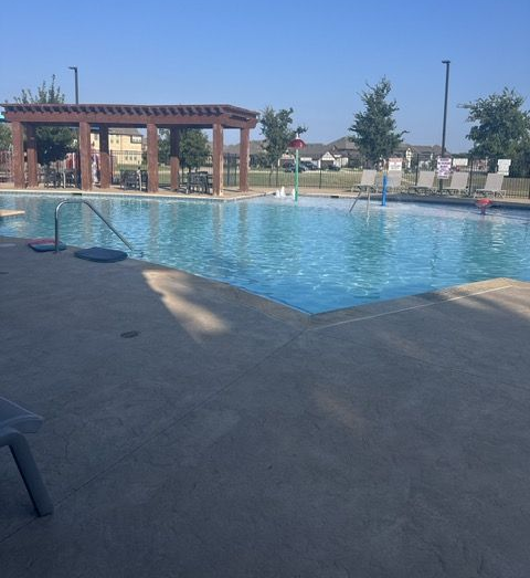 Outdoor swimming pool with blue water, shaded pergola, and lounge chairs on a sunny day