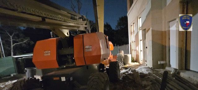 Orange utility truck parked by a building at night, with debris and snow on the ground