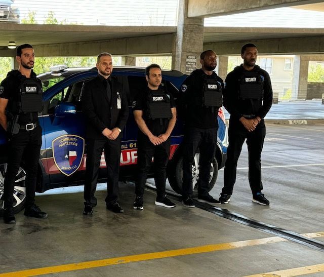 Five security officers in black uniforms stand beside a police-style shield in a parking garage.