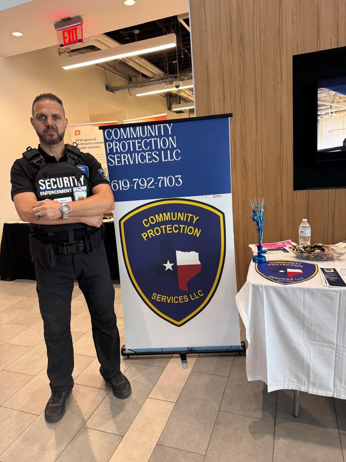 Security guard standing beside a community services banner and table in an indoor lobby.