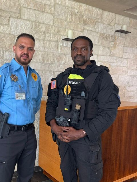Two security officers in uniform standing indoors beside a wooden counter and stone wall