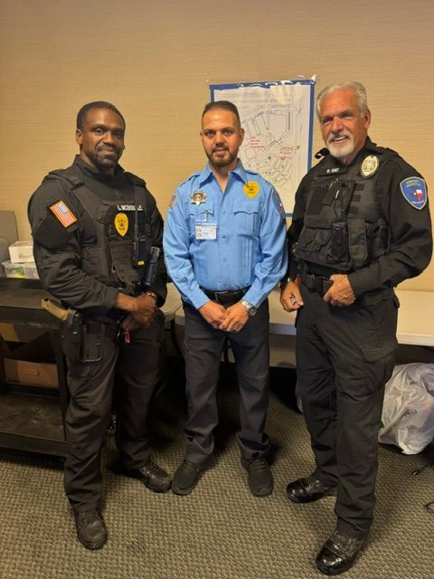 Three security officers standing indoors, wearing black and blue uniforms.