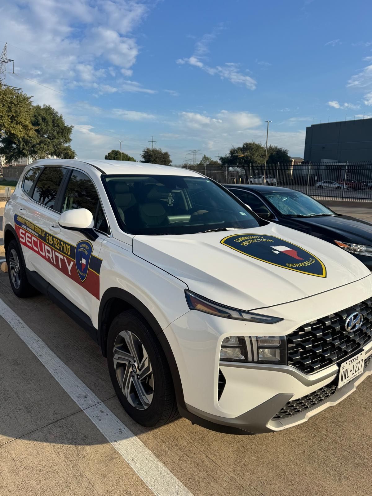 White police SUV parked outdoors in a lot, with blue-and-red decals and a shield emblem on the door.