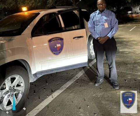 Man standing beside a white security SUV with a shield logo, parked at night in a lot.