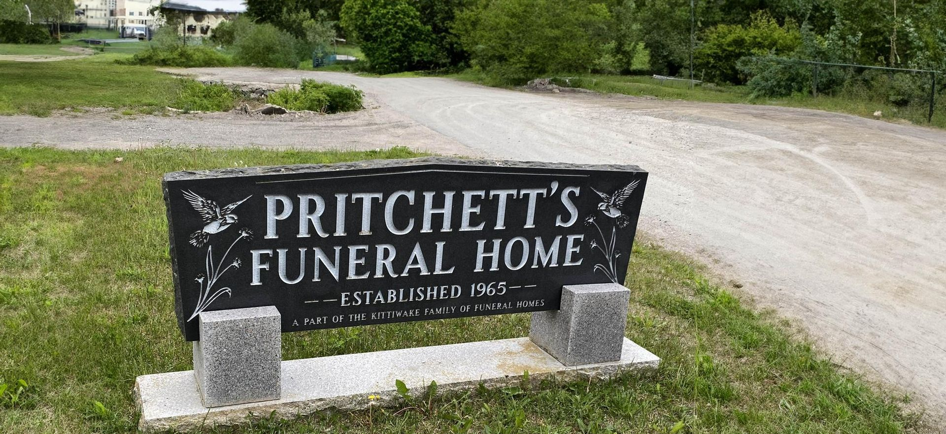 Pritchett’s Funeral Home sign beside a gravel driveway and green trees
