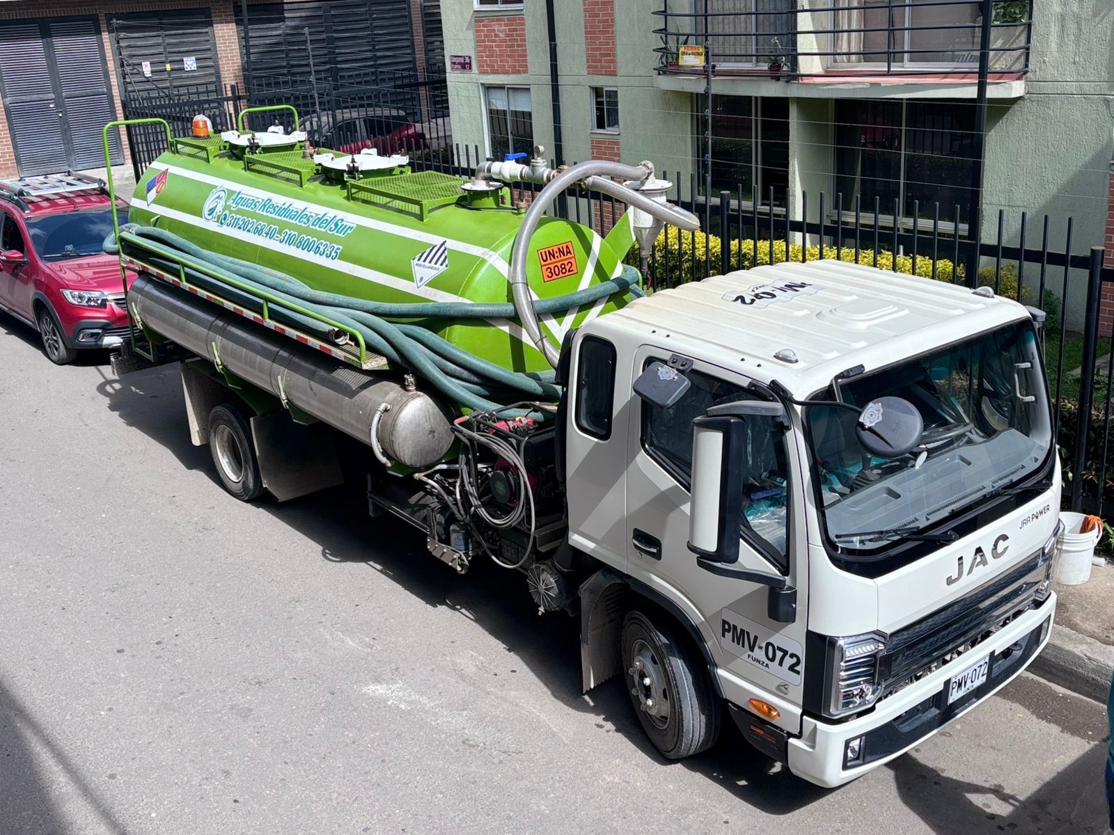 Camión séptico verde y blanco estacionado en una calle cerca de un edificio