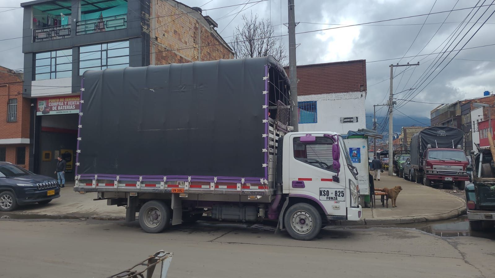 Un camión estacionado con una lona negra en una calle frente a edificios.