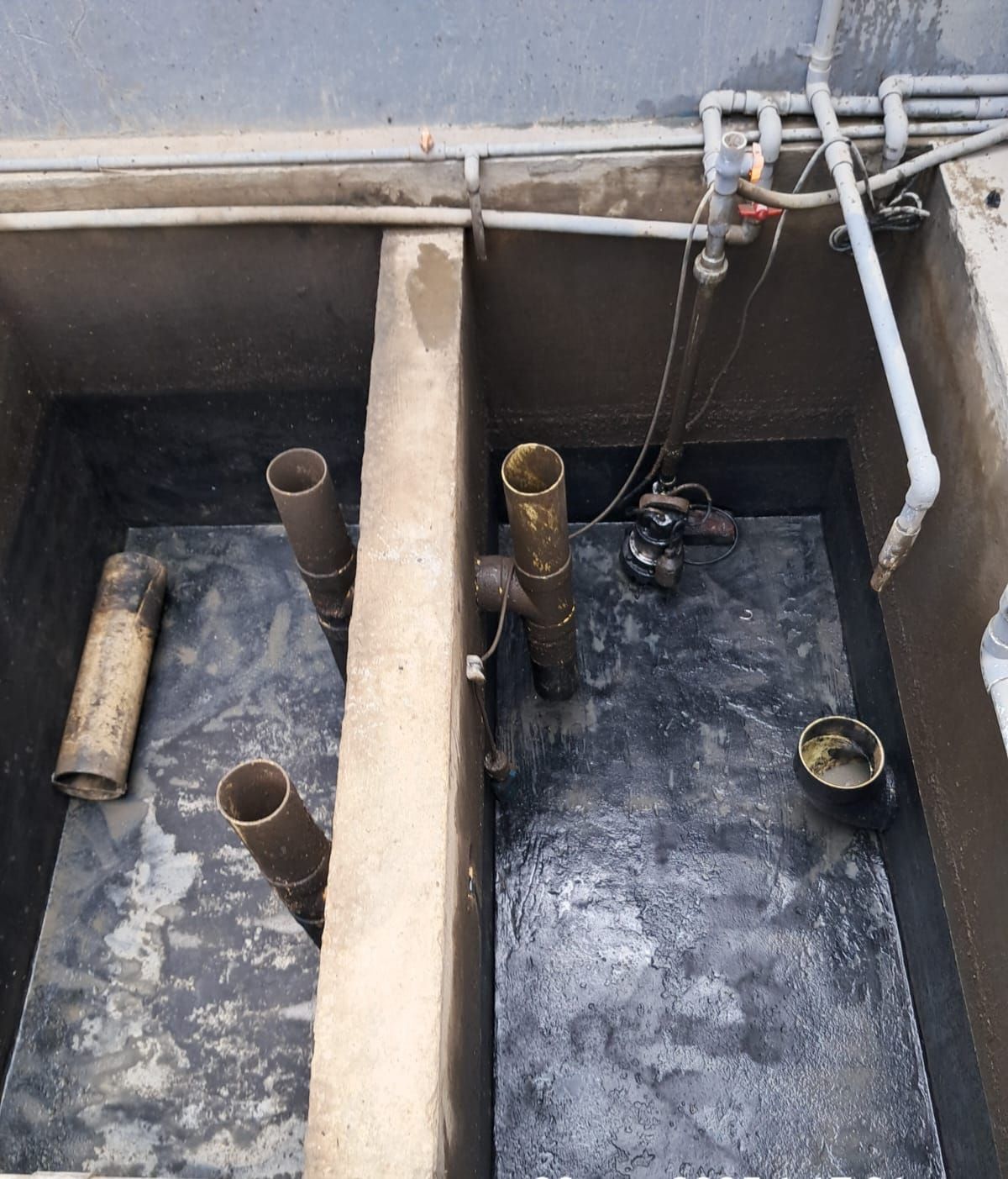 Un tanque séptico de dos cámaras con tuberías y plomería visibles, paredes interiores negras y divisores de concreto.
