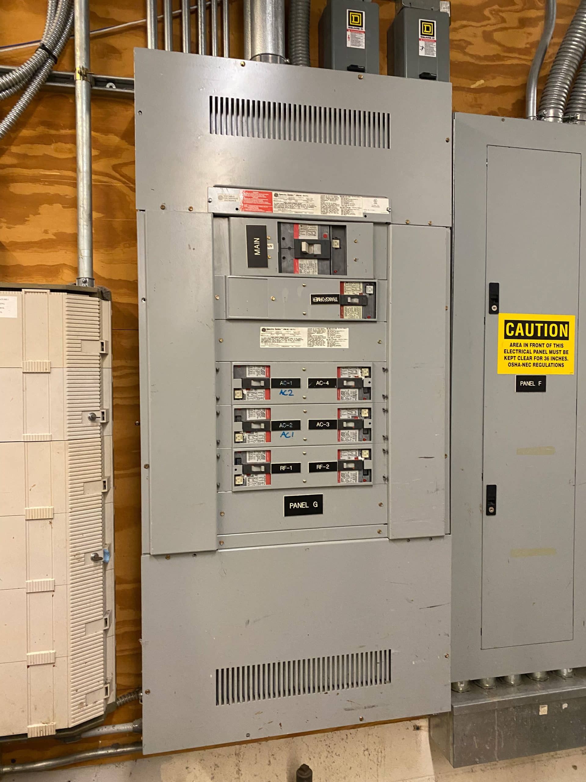 Electrical panel with circuit breakers. Gray metal panel mounted on a wall with conduit and wiring visible.