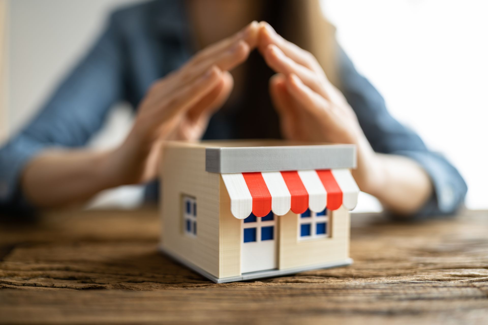 Hands shielding a small model storefront with a red striped awning.