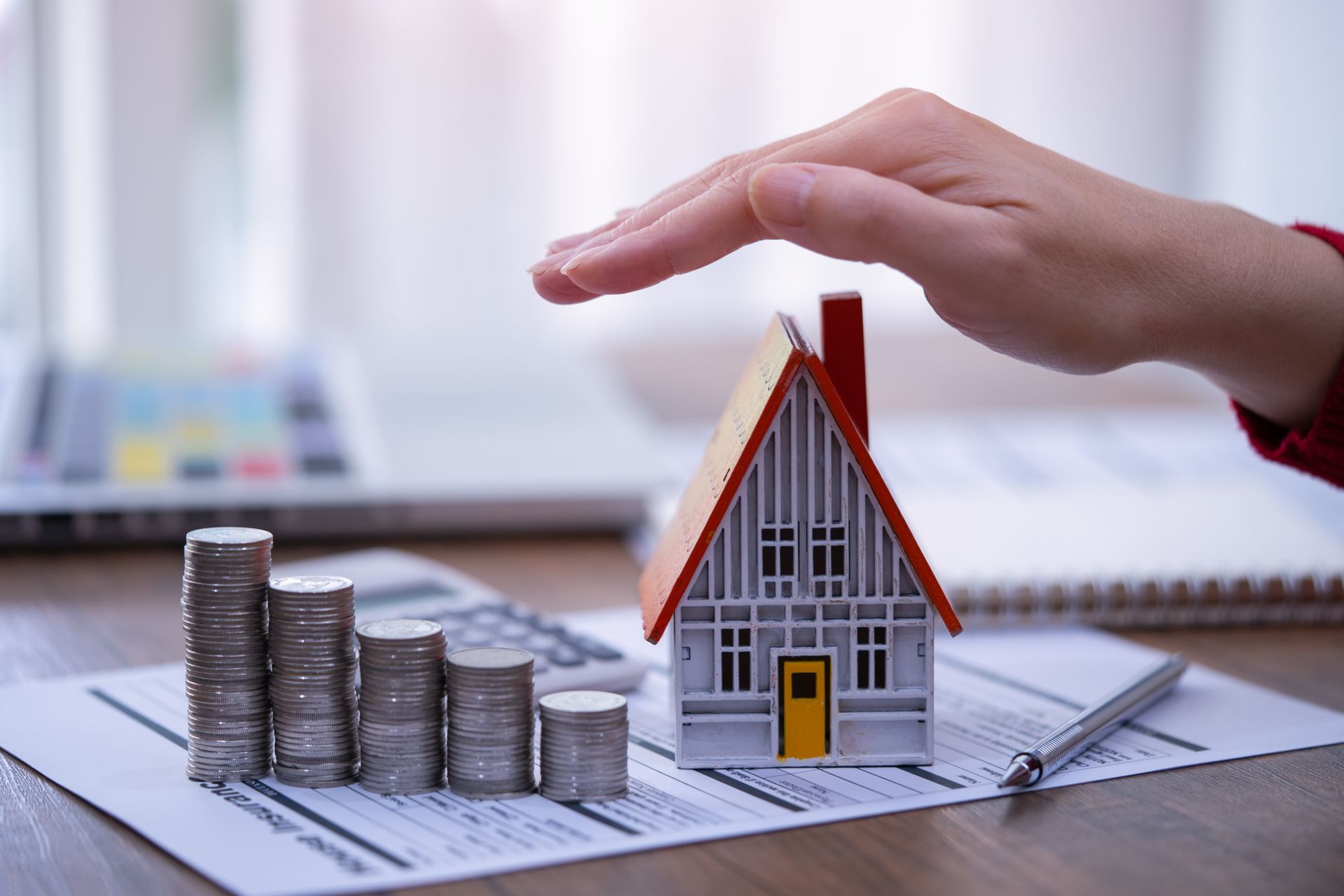 A person is covering a model house with their hand.