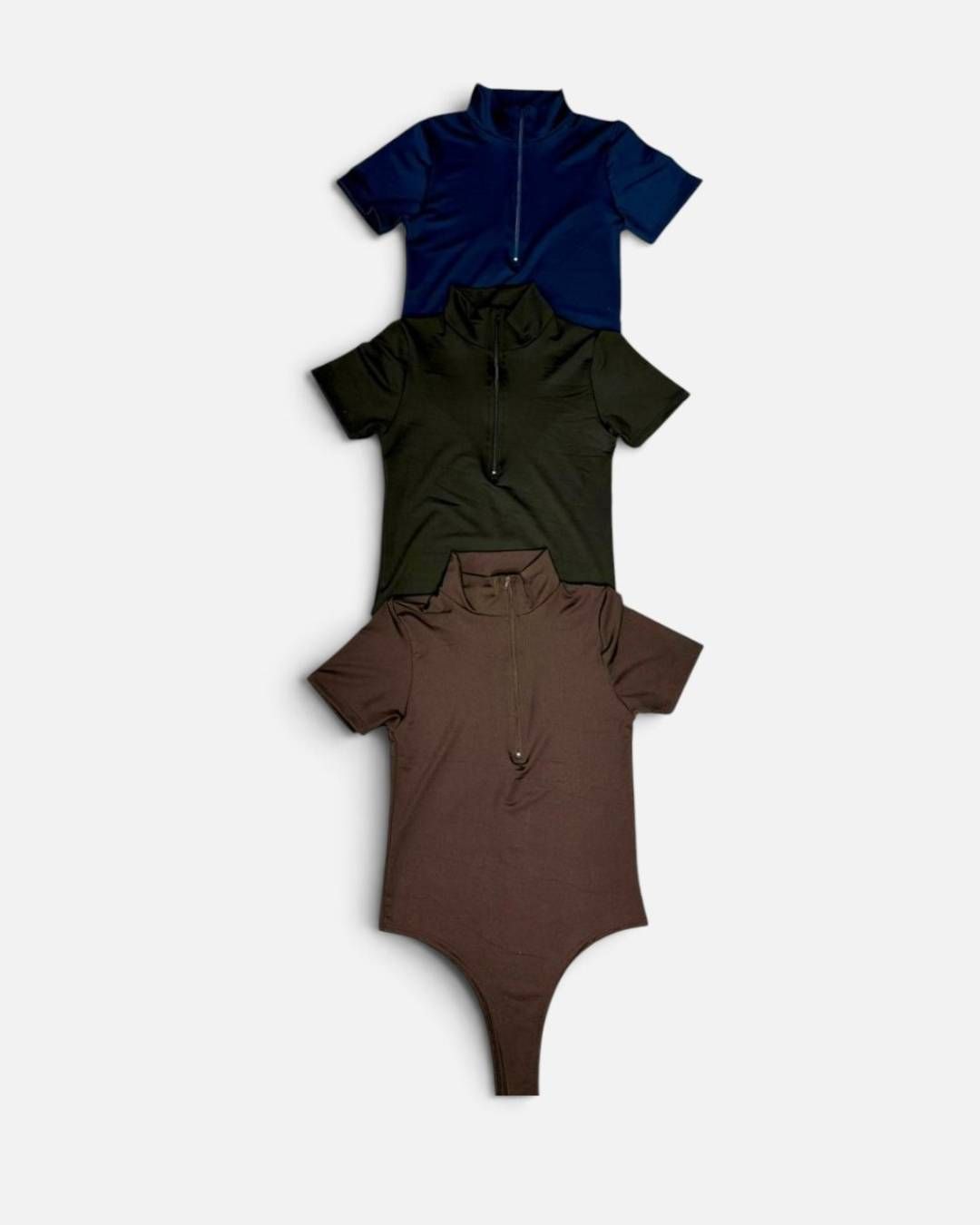 Tres bodys de manga corta con botones en azul marino, verde oliva y marrón, dispuestos verticalmente.