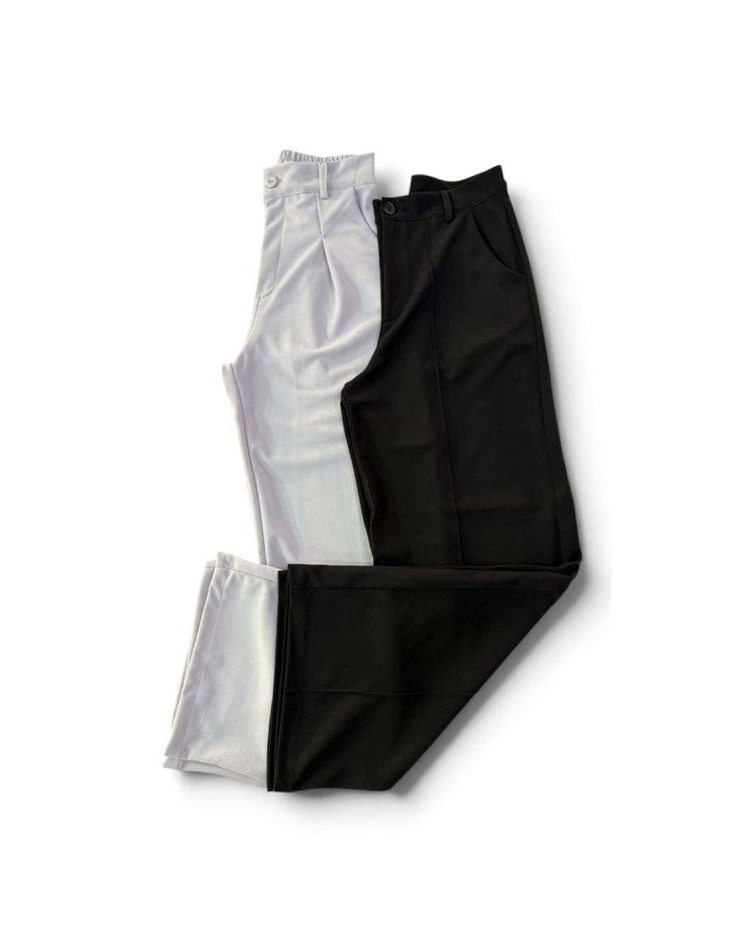 Dos pares de pantalones doblados, uno gris claro y otro negro, apilados sobre un fondo blanco.