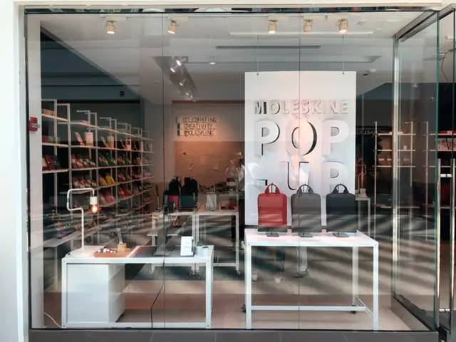 A store window with a sign that says ' moleskine pop up ' on it.