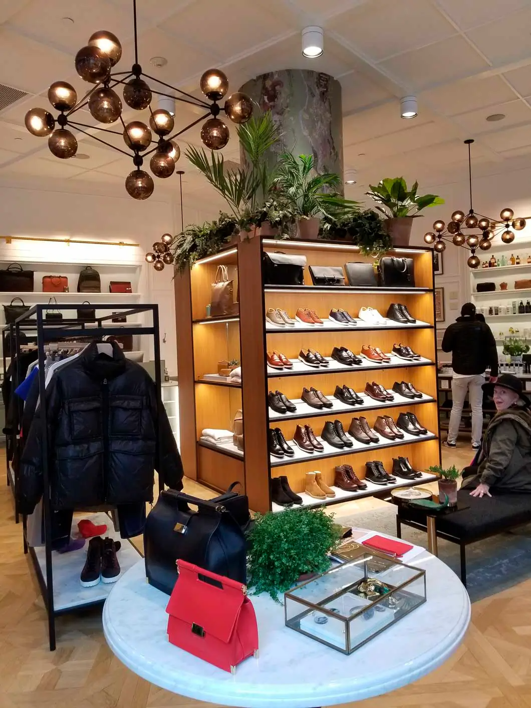 A man sits on a bench in a store looking at shoes