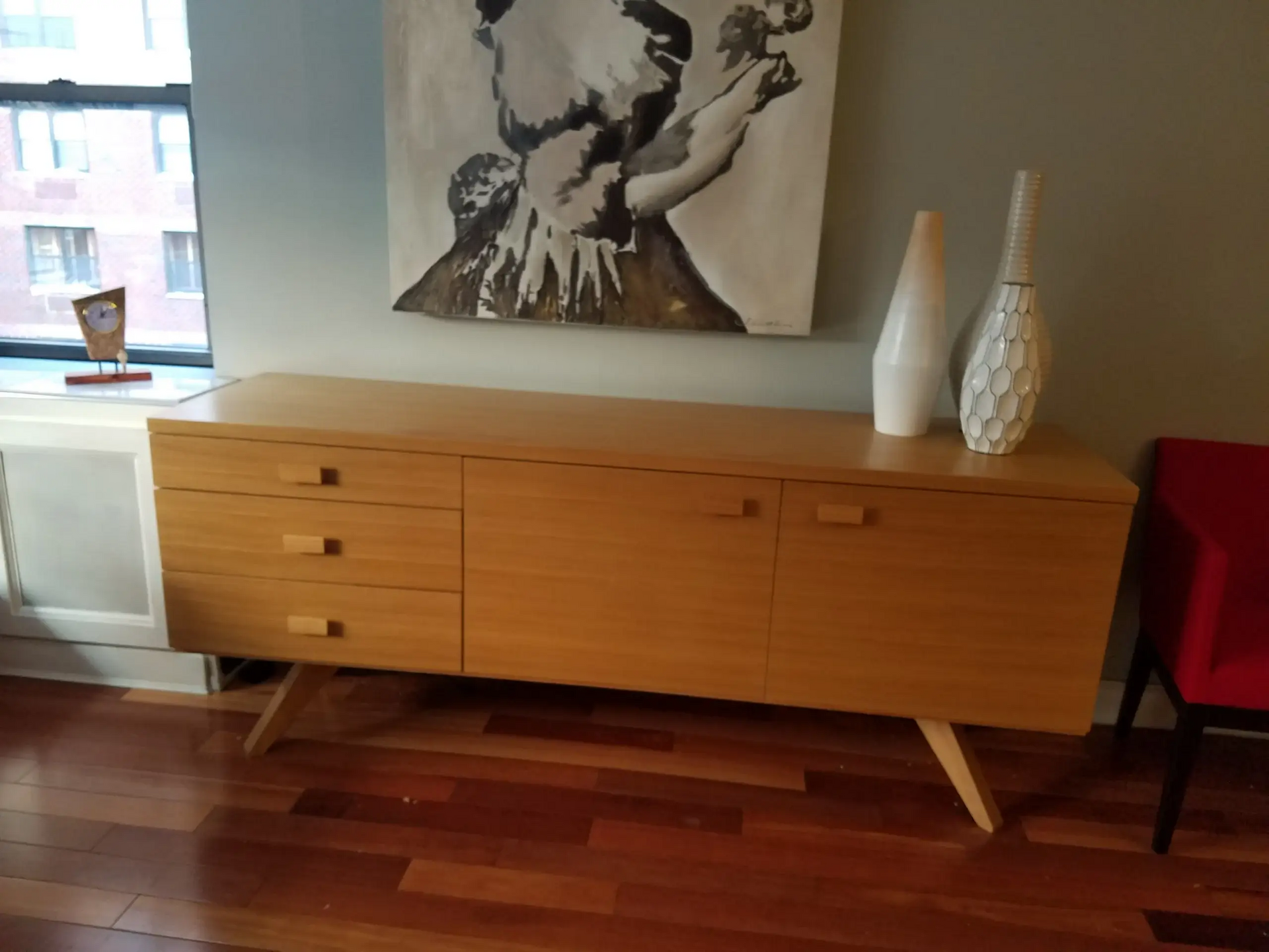 A wooden dresser with a painting on the wall above it