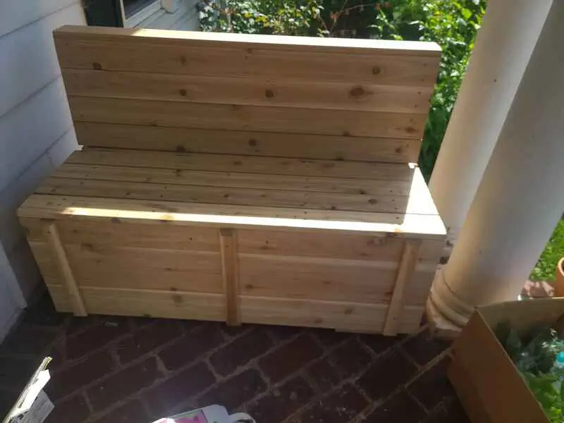 A wooden bench is sitting on a porch next to a planter.