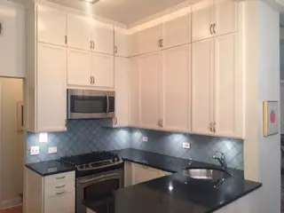 A kitchen with white cabinets , black counter tops , a stove , microwave and sink.