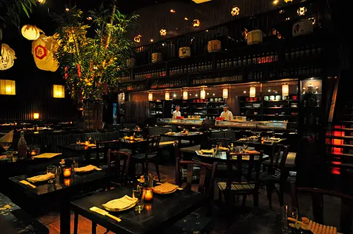 A restaurant with a lot of tables and chairs and a chef in the background.