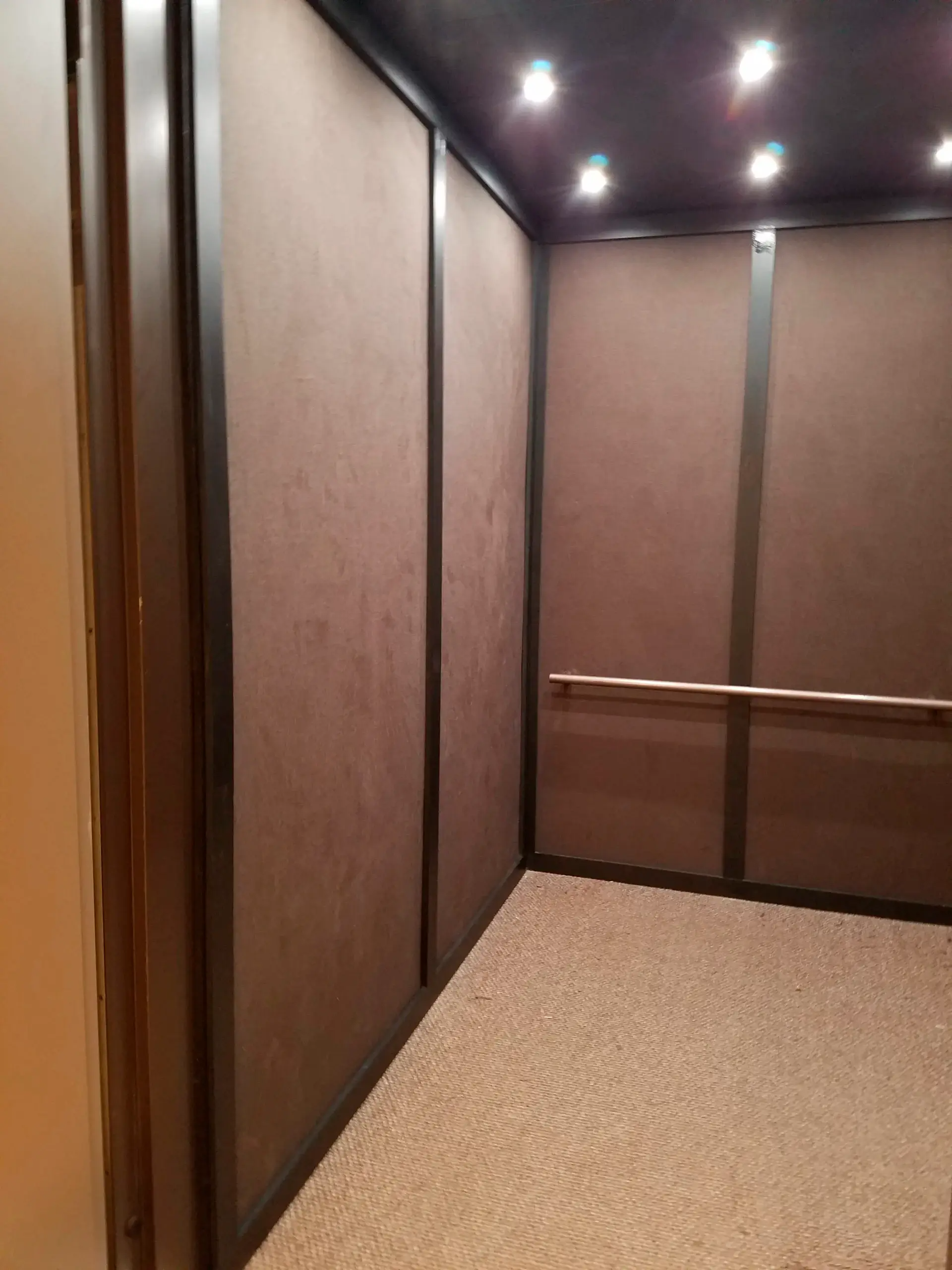 An empty elevator with brown walls and a carpeted floor.