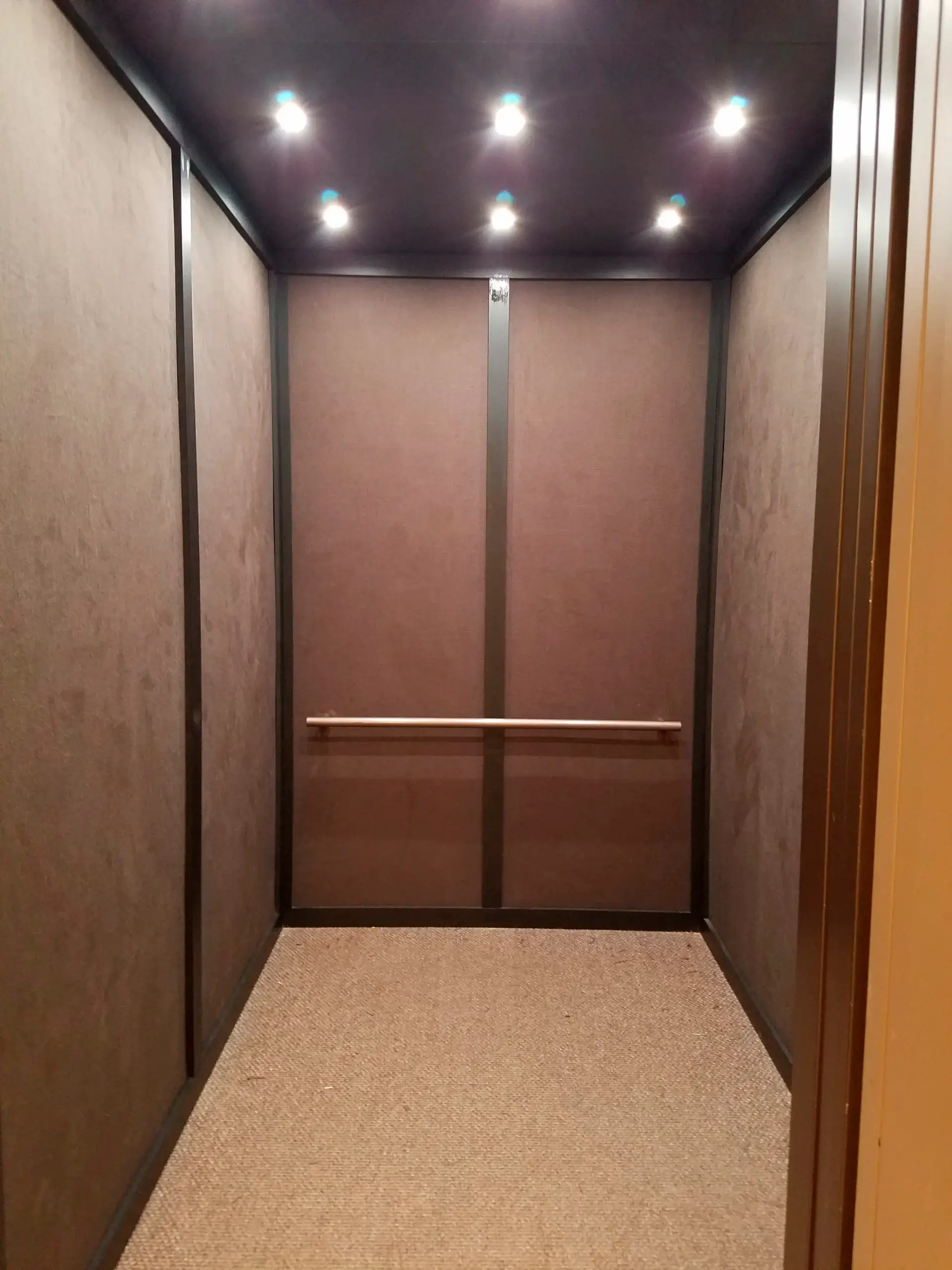 An empty elevator with brown doors and a ceiling light.