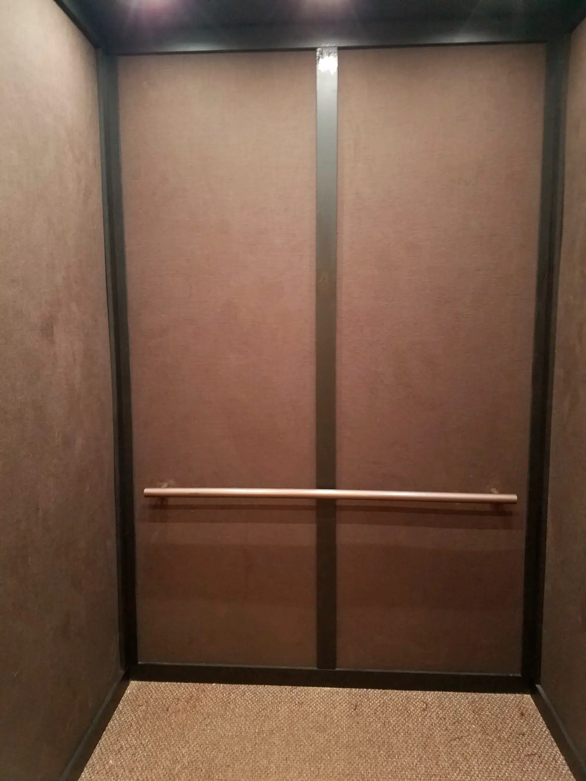 The inside of an elevator with brown walls and a wooden handle.