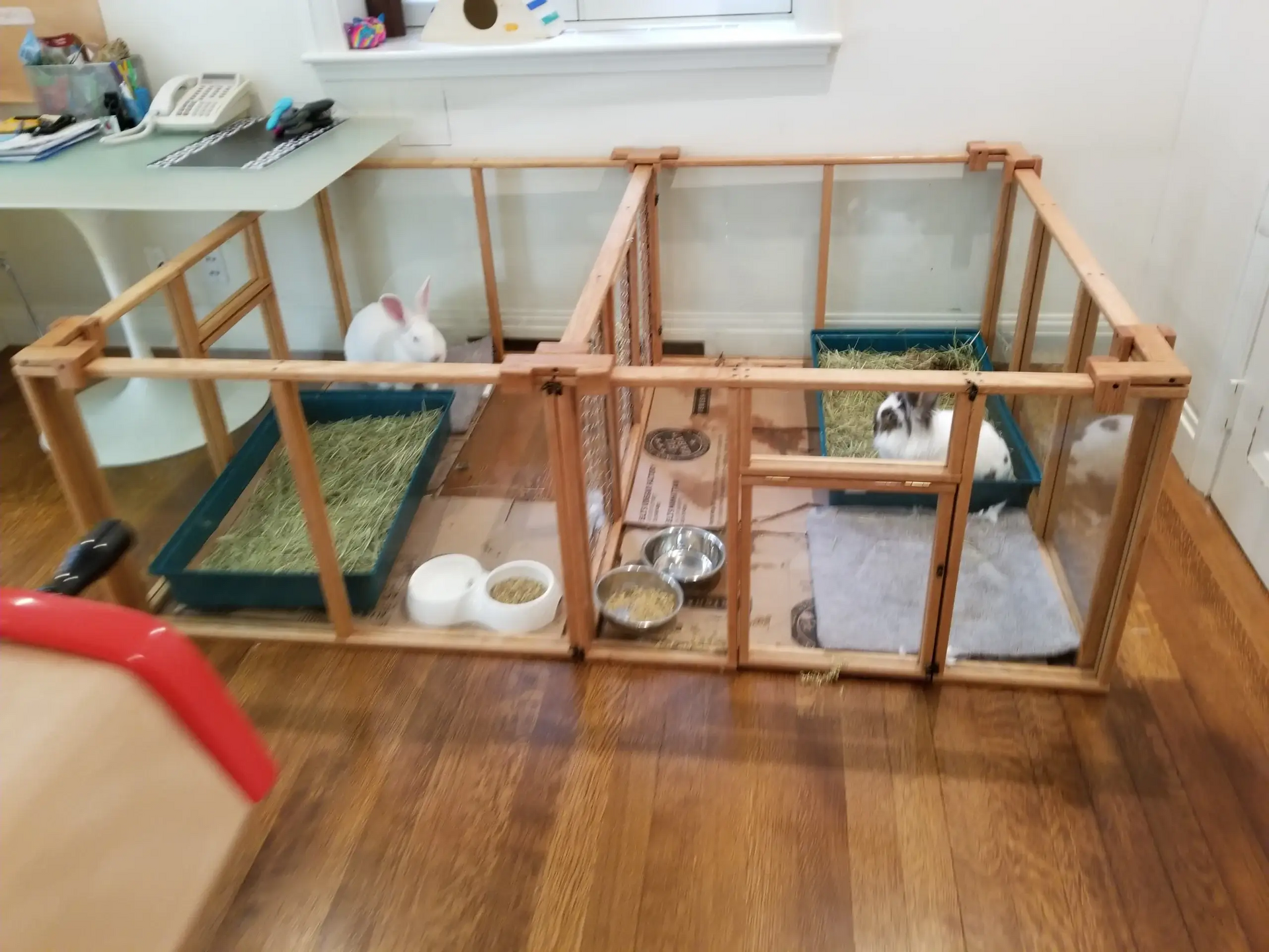 Two rabbits are sitting in a wooden cage on a wooden floor.