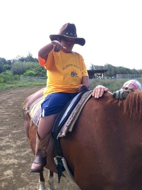 A boy in a yellow shirt is riding a brown horse