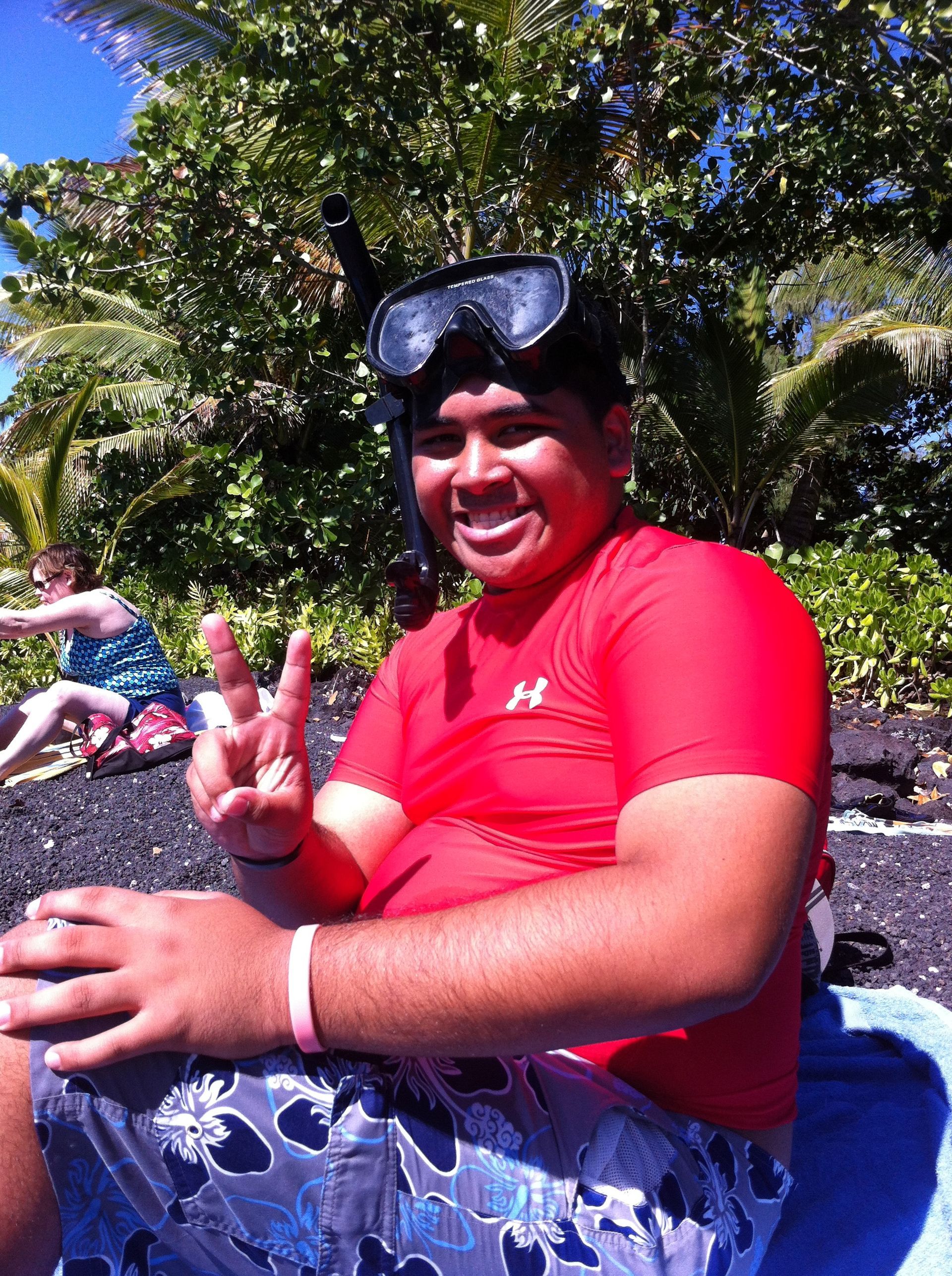 A man wearing a red shirt and goggles is giving a peace sign