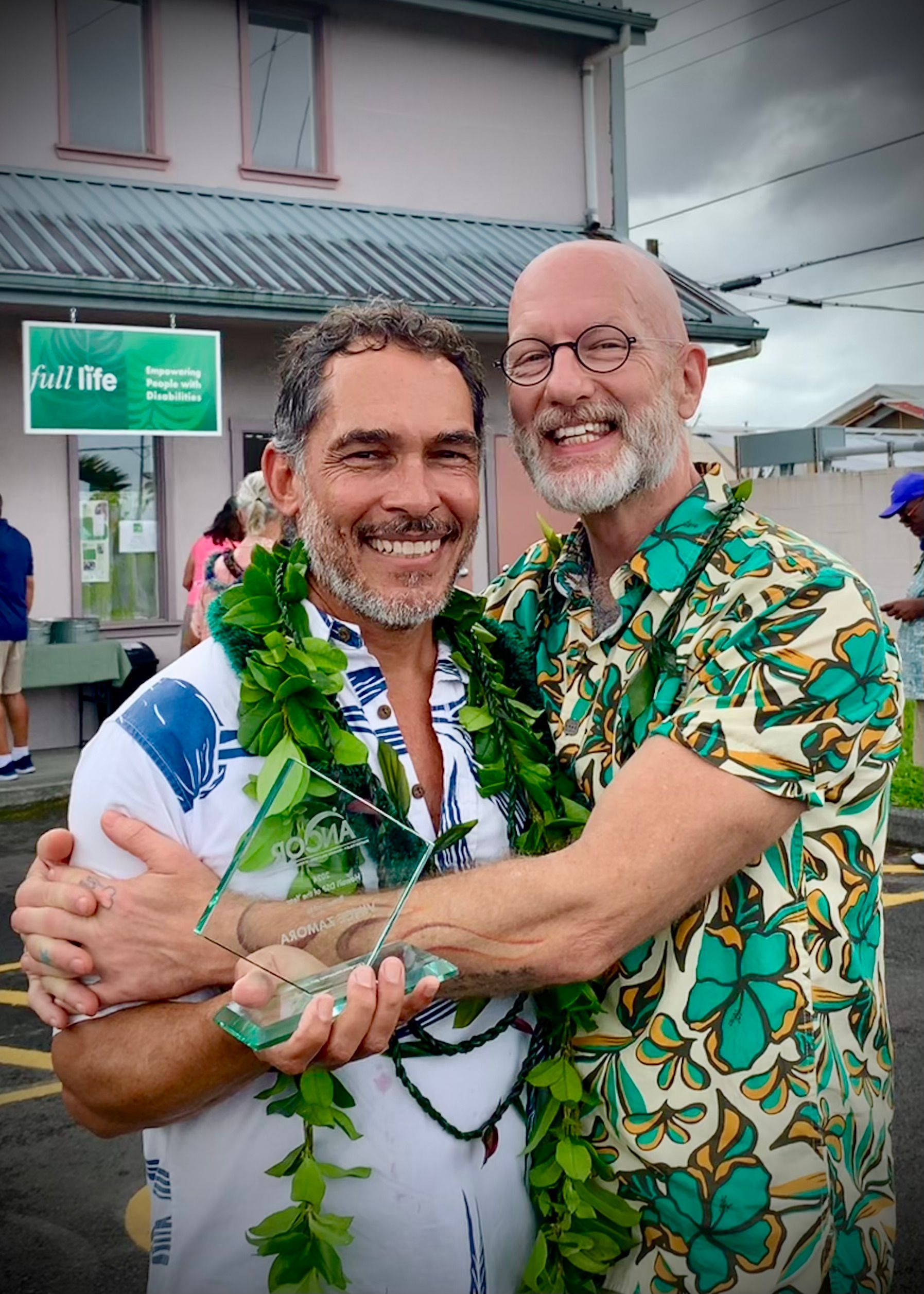 Two men are hugging each other and one is holding a trophy