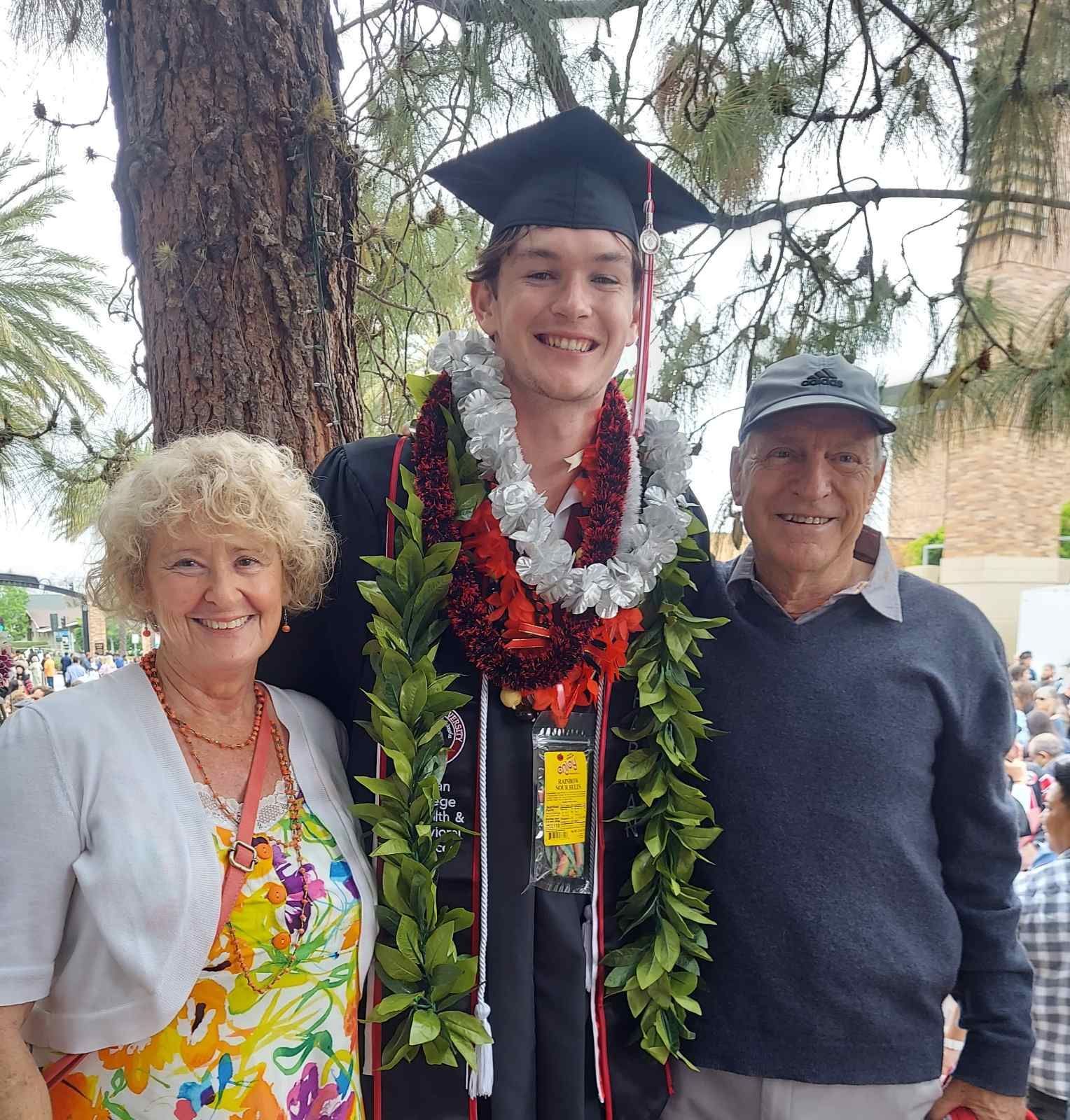 A man in a graduation cap and gown is posing for a picture with his parents