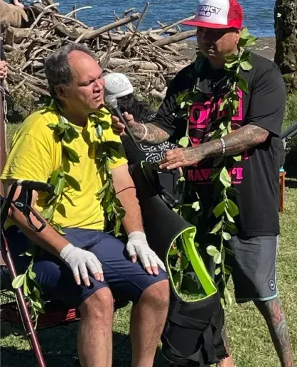 A man wearing a lei is sitting next to another man wearing a lei.