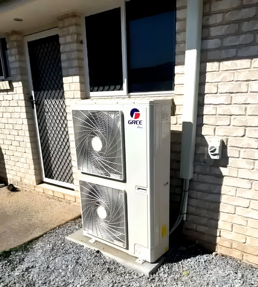 A White Air Conditioner Is Sitting Outside Of A Brick Building — Davey Service & Maintenance Qld In Clinton, QLD