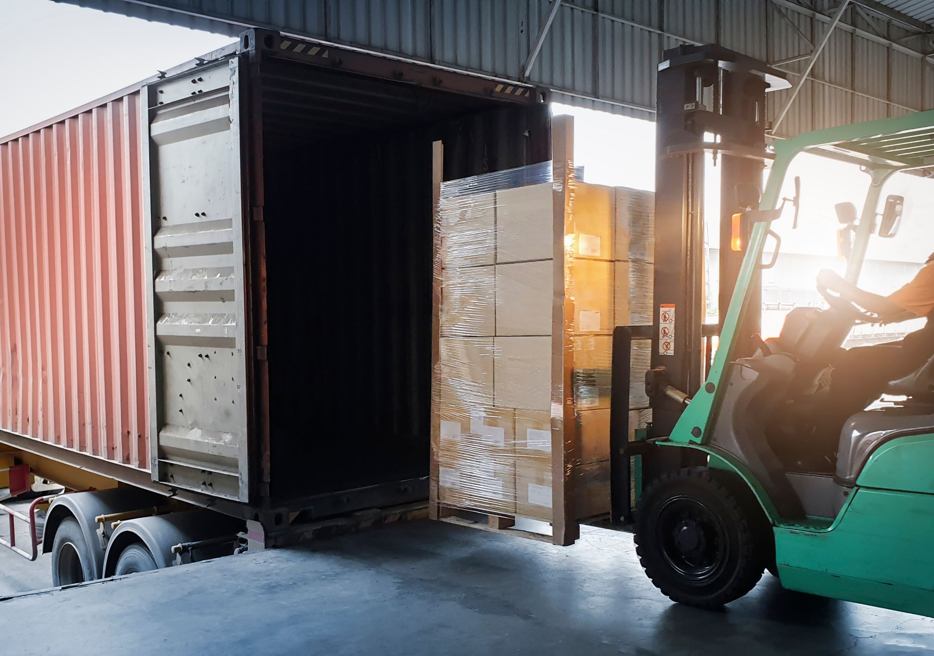 Forklift loading boxes into a shipping container at a warehouse.