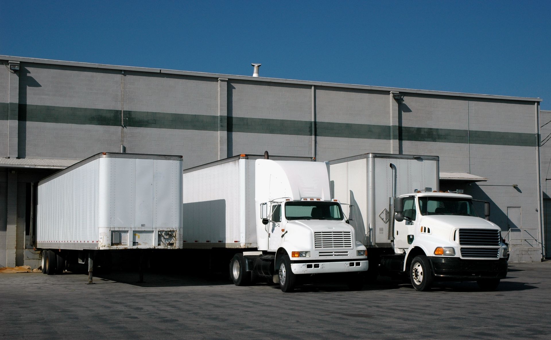 Trucks parked at a loading dock of a gray industrial building, ready for loading and unloading cargo.