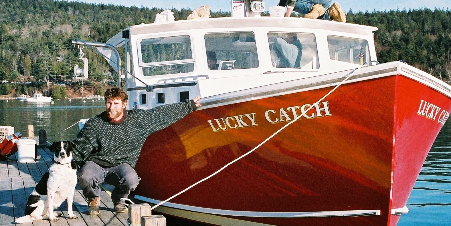 Man and dog pose on a dock next to a red fishing boat named 