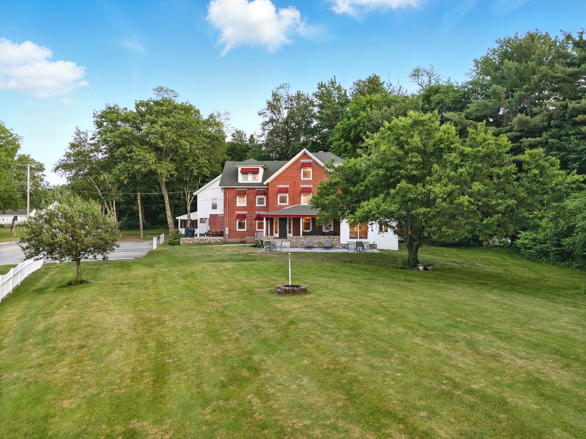 A two-story red brick and white farmhouse with a large grassy front yard, surrounded by trees.