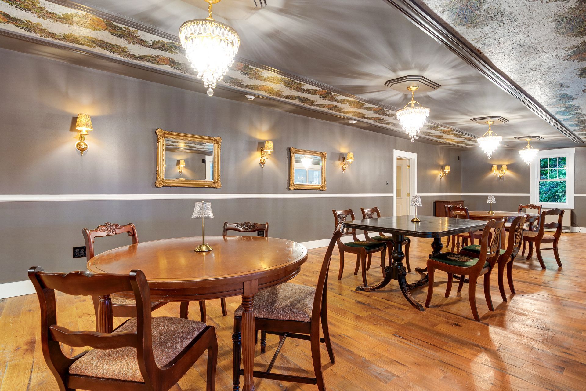 Formal dining room with wood floors, tables, chairs, ornate chandeliers, and sconces.