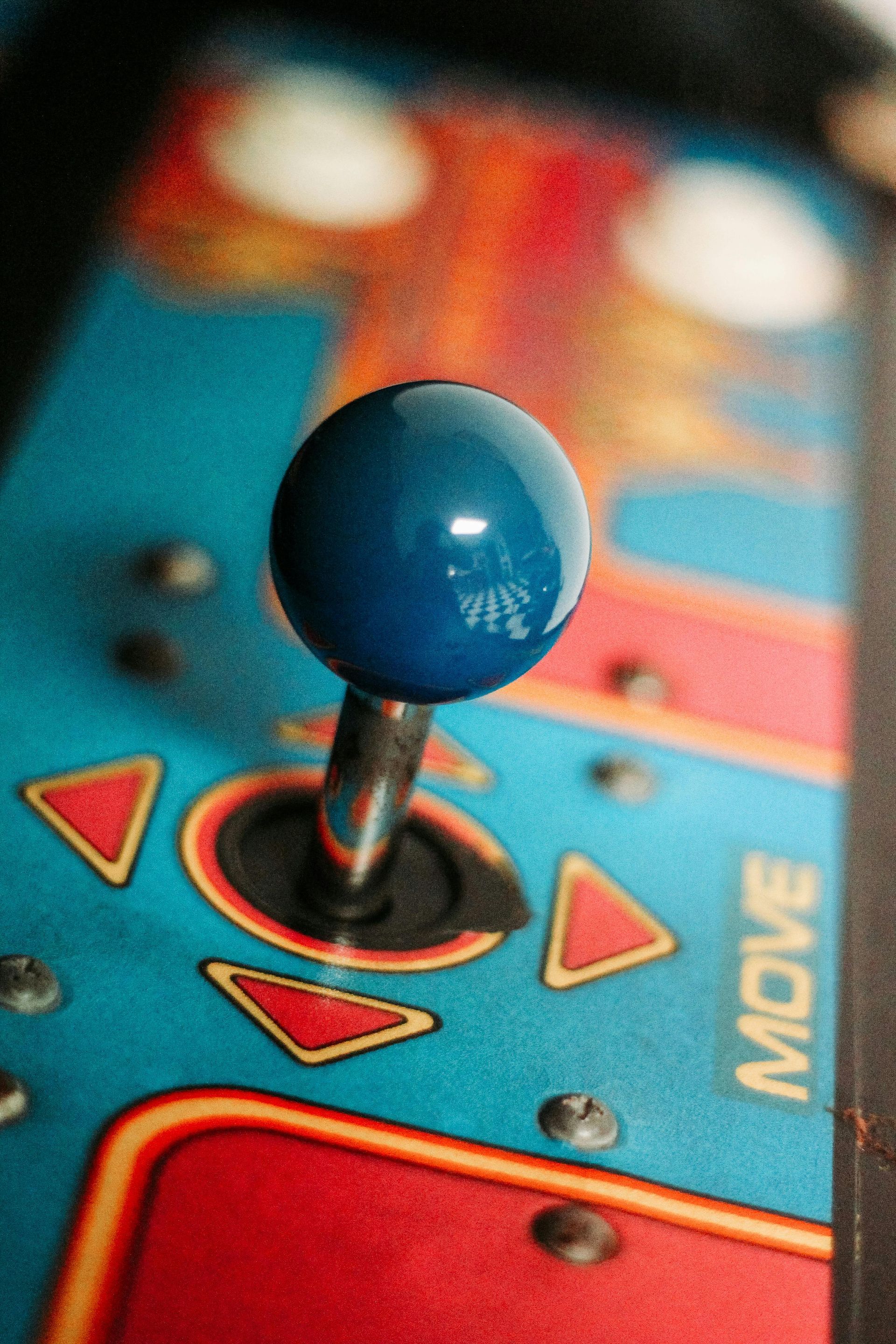 Blue joystick on a teal arcade control panel with red triangle buttons and the word 