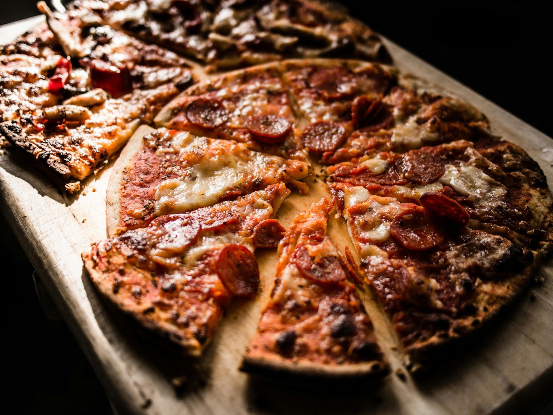 Pizza slices on a wooden board, including pepperoni and other toppings.