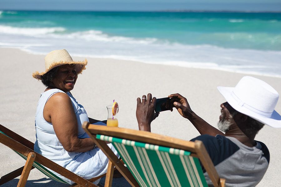 Two people relaxing in beach chairs, wearing sun hats, and taking a photo by the ocean.