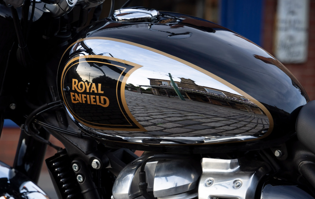 Close-up de um tanque de combustível preto brilhante para motocicleta Royal Enfield com logotipo dourado e reflexos.
