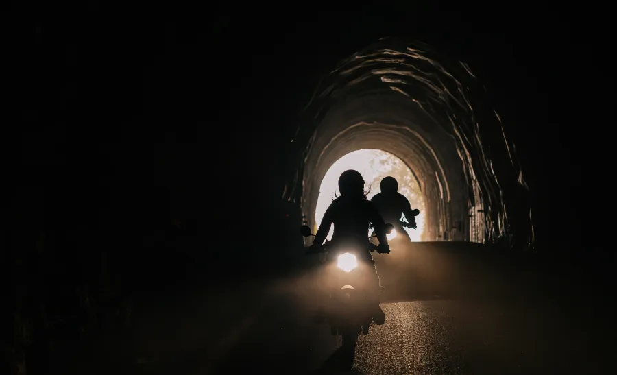 Silhueta de uma pessoa carregando uma criança através de um túnel escuro em direção a uma saída iluminada.