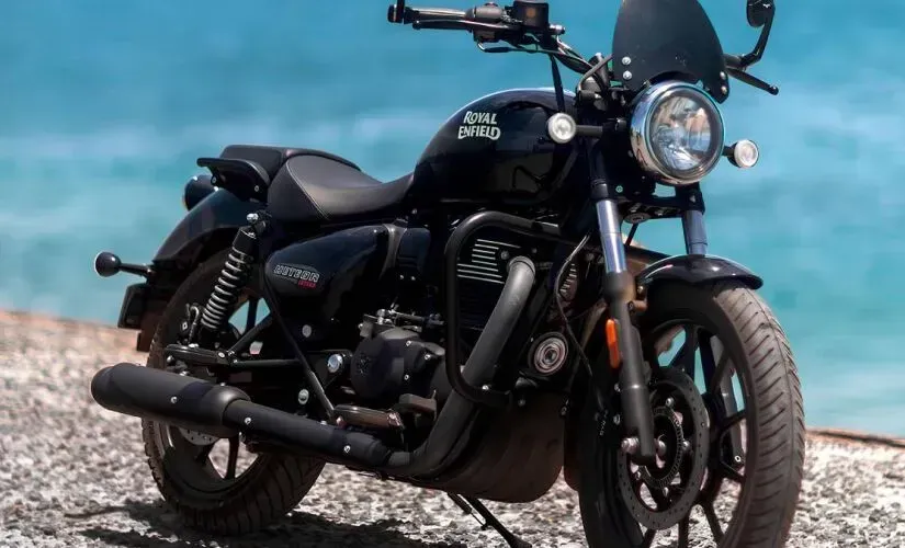 Motocicleta preta estilo cruiser estacionada em uma costa rochosa com água azul ao fundo.