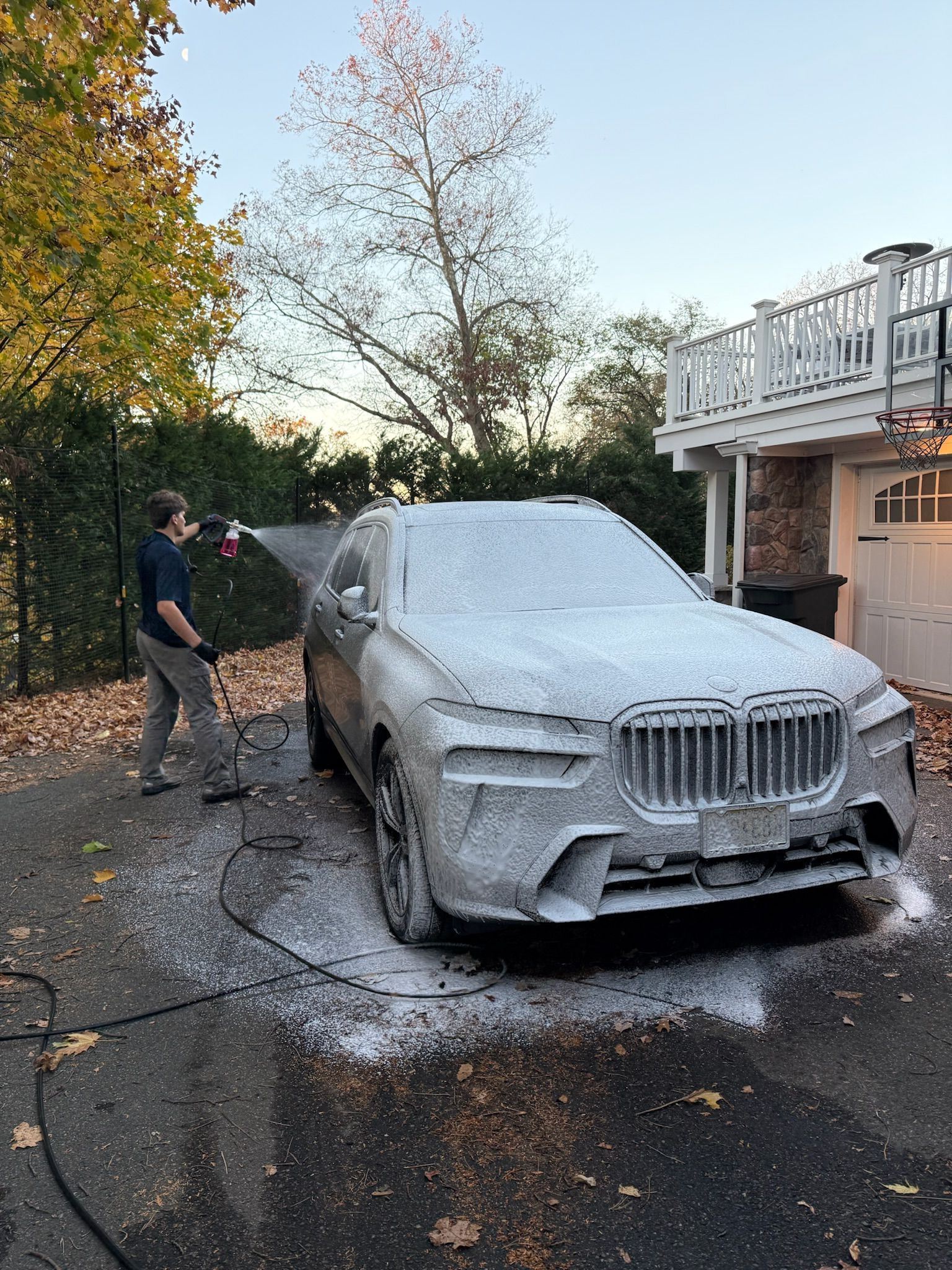 A man is washing a car with foam in a driveway.